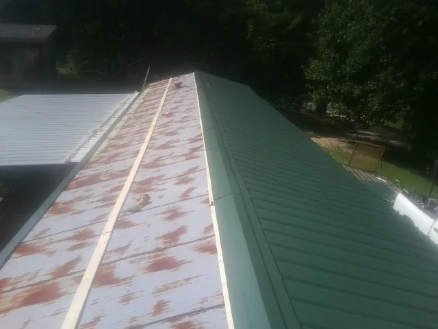 Old rusted panels beside newly installed green metal roofing — Wind Damage Roof Repair by Roofing Brothers in Newberry
