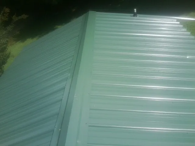 New green metal panels meeting at the ridge of a roof — Flat Roof Repair work by our crew in Newberry