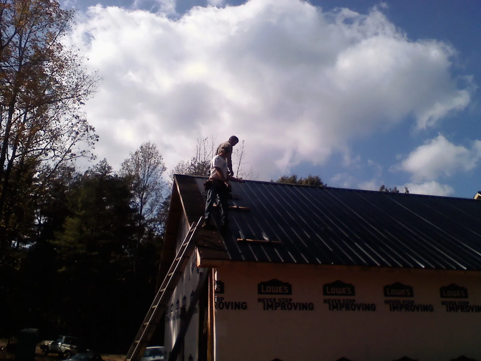 Roofer fastening dark metal panels high against a cloudy sky, from a Roof Inspection job in Newberry