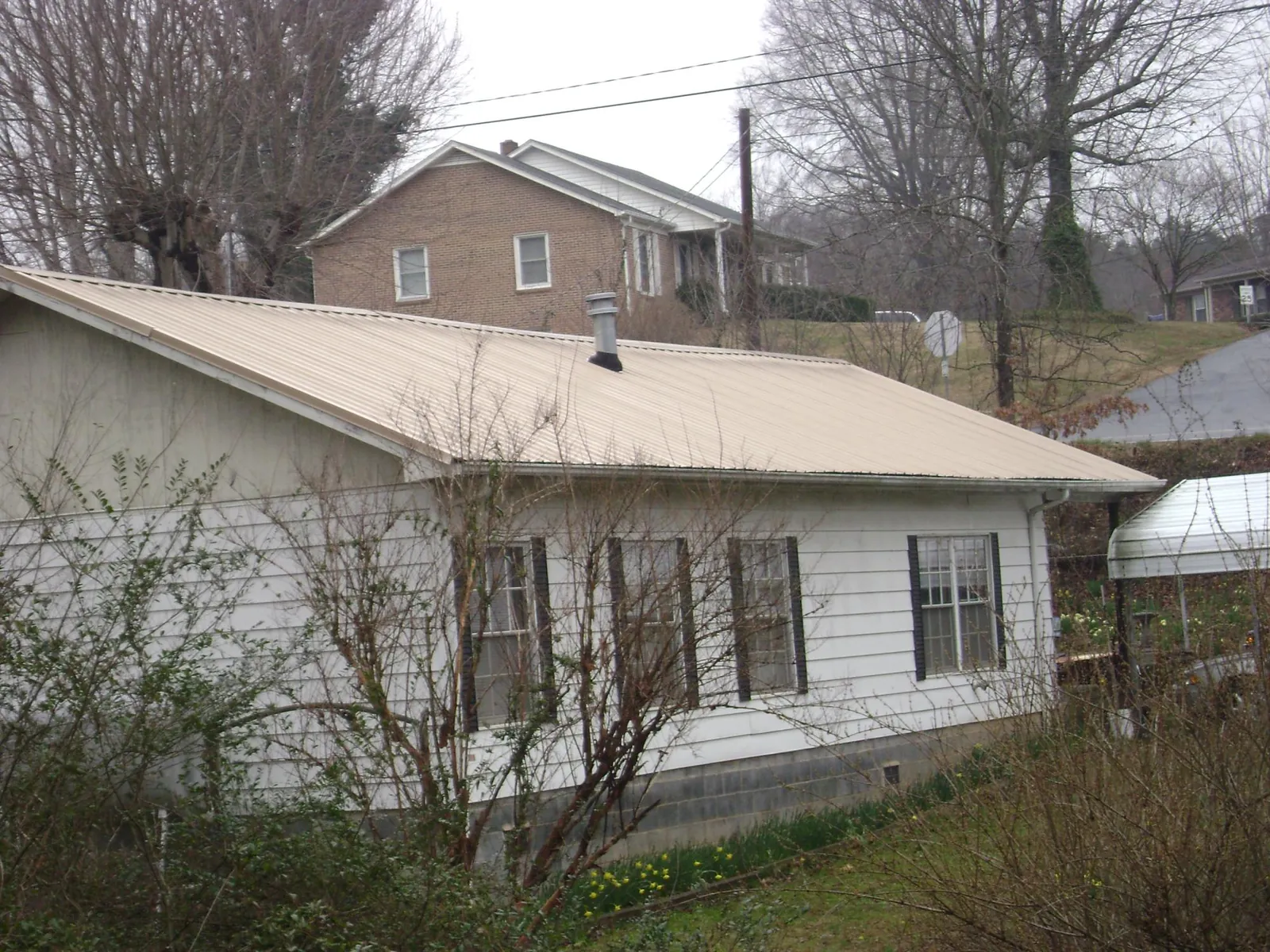 Tan metal roof on a white sided house set into a hillside — Commercial Roofing by Roofing Brothers in Newberry