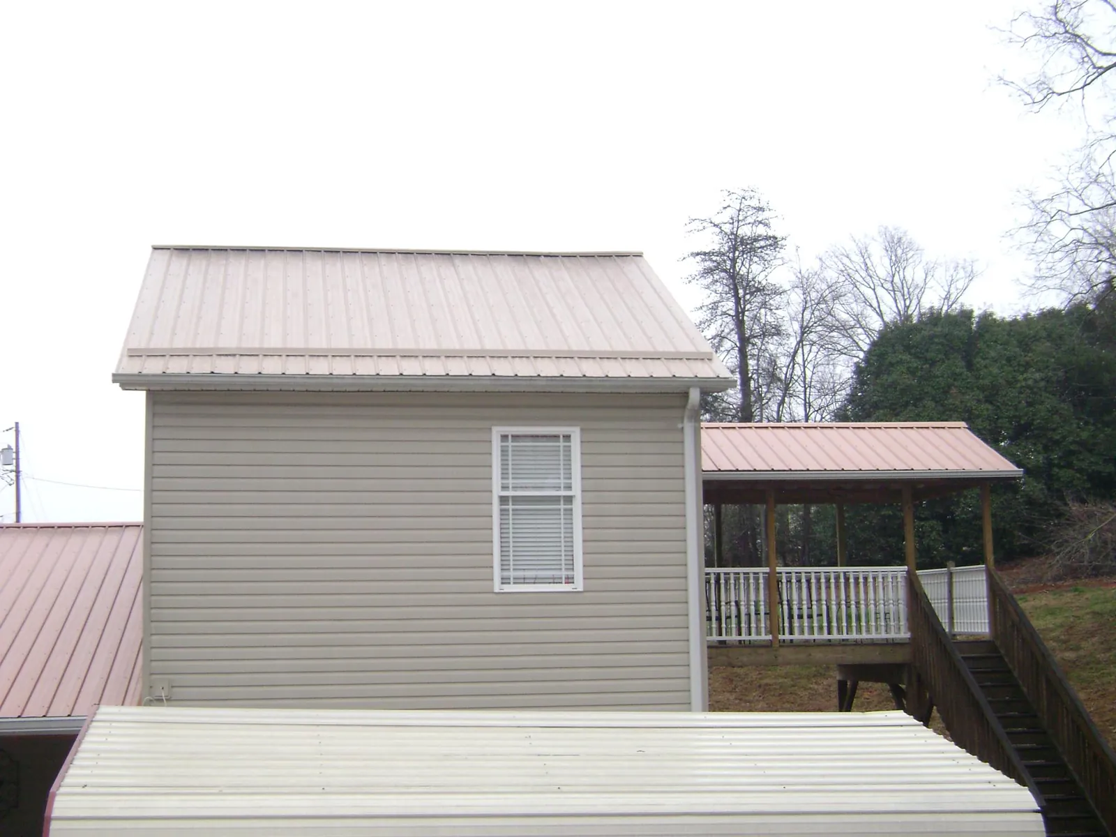 Tan metal roofs on a two story addition and attached porch, from a Roof Replacement job in Newberry